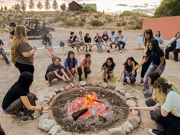 a group of campers roasting marshmellos around the firepit